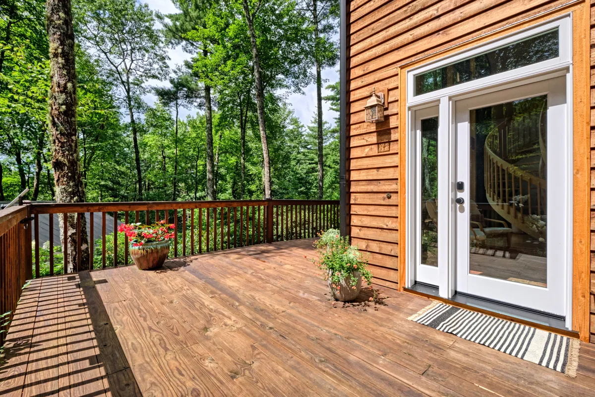 A tranquil deck surrounded by planters and mature trees, with large glass doors connecting the indoor and outdoor living spaces. The golden hour light hints at the onset of evening, and the serene mood evokes the transition from day to night.