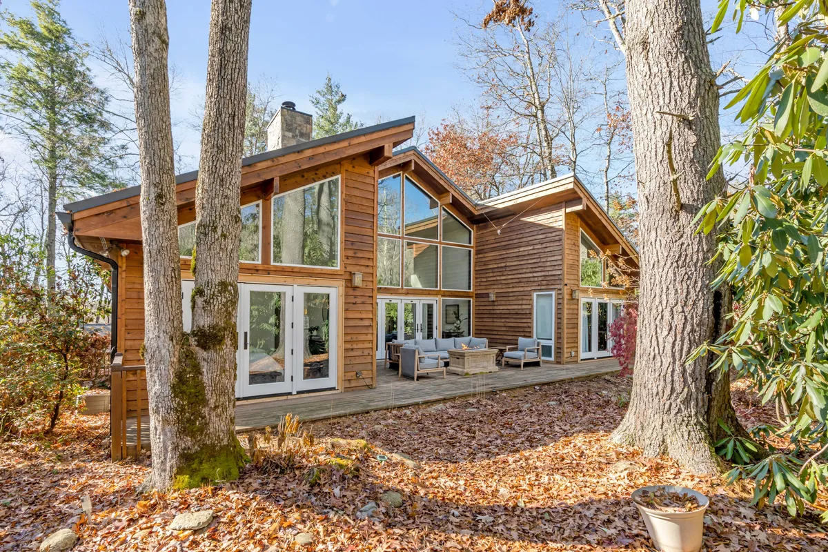 This image captures the exterior of the Sunlight Chalet, featuring large glass windows, a wooden exterior, an inviting outdoor seating area, and lush trees surrounding the home. The scene exudes a cozy and serene mood, ideal for enjoying a sunrise coffee or an evening of star-gazing after a day in town.