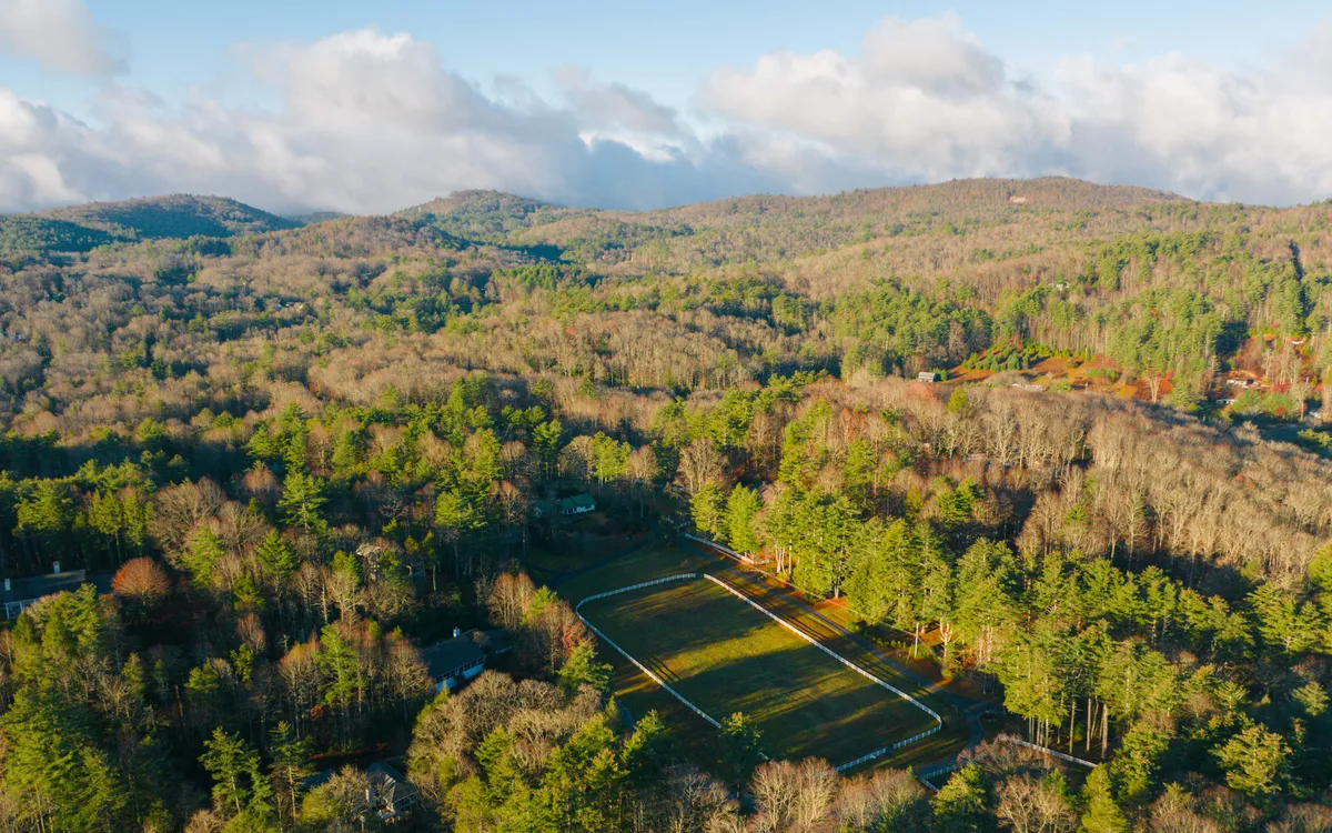 An expansive green field flanked by mountains and dense forest, evoking the grandeur and tranquility of the natural setting. The view is open and inviting, ideal for hiking, picnicking, and appreciating the wilderness.