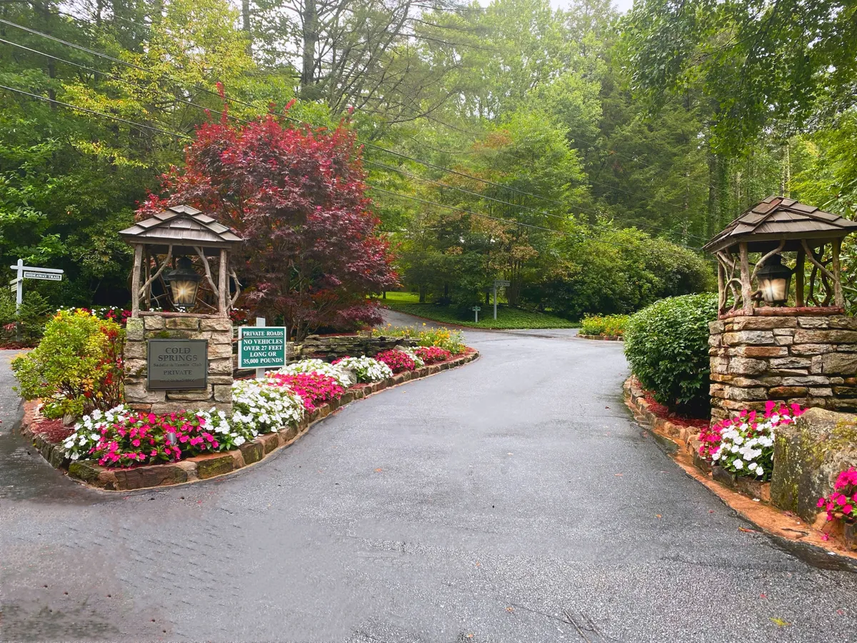 A picturesque stone entrance surrounded by colorful flower beds and wooden lantern structures creates a welcoming arrival scene. The garden and landscaping offer a vibrant, inviting first impression, hinting at the beauty and sophistication of the area.