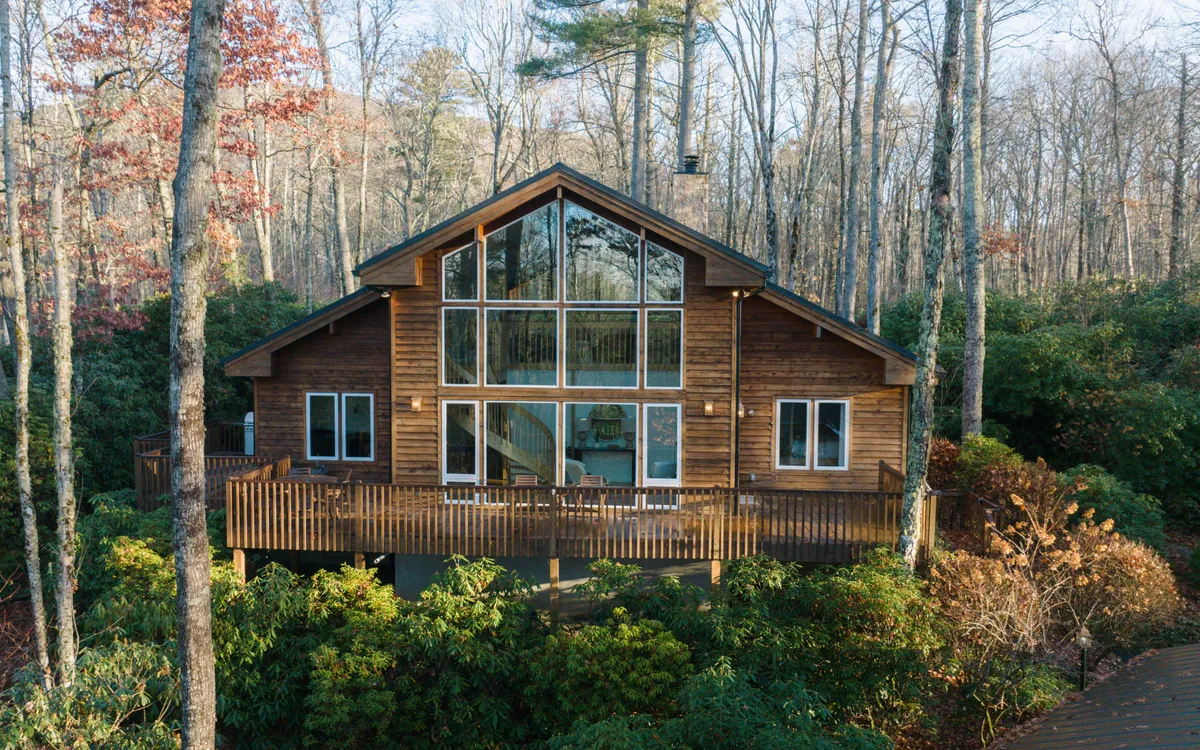 This image highlights Sunlight Chalet's impressive exterior, featuring large glass windows, a wooden deck, and lush surrounding greenery. The structure’s unique winged layout is showcased, with the deck inviting outdoor relaxation and group gatherings against a backdrop of tranquil forest.